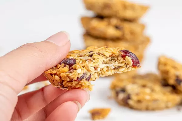 Close-up, a piece of oatmeal cookies with seeds and raisins in a woman's hand