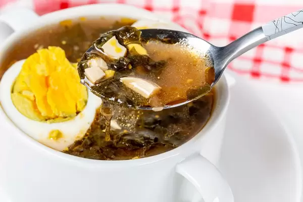 Close-up, a spoon with red soup with eggs and herbs