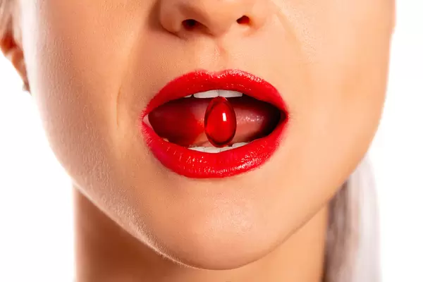 Close-up, a woman with an open mouth holds a red capsule in her teeth