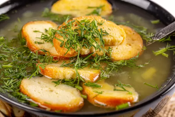 Close-up, black bowl of soup with croutons and dill greens