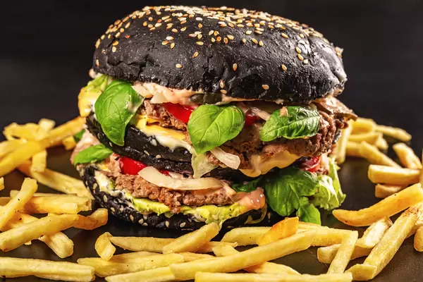 Close-up, black burger with two cutlets, cheese, vegetables and herbs and french fries