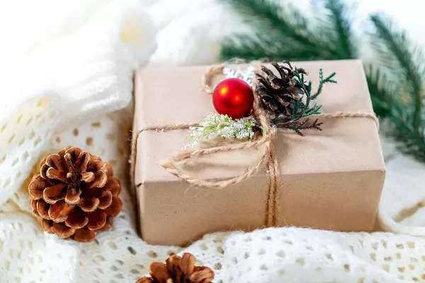 Close Up Bokeh Photo of Christmas Gift Box next to pinecones on white knitted blanket