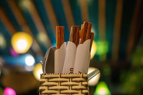 Close Up Bokeh Photo of Cutlery Holder Basket with Spoons, Forks and Wooden Chopsticks in Paper Wrappers in a Restaurant