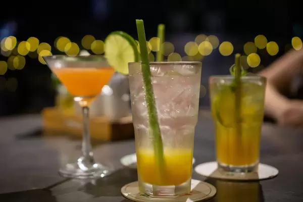Close Up Bokeh Photo of different Cocktails and Mocktails in Martini and Cocktail Glasses with Ice Cubes and Lemongrass Straws on a Rooftop Bar with Lights in the Background