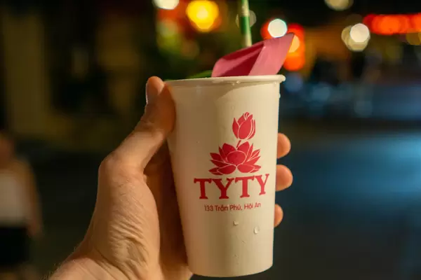 Close Up Bokeh Photo of Person holding a Paper Cup of Herbal Tea with Lotus Leaves and Paper Straw in the Ancient Town of Hoi An, Vietnam