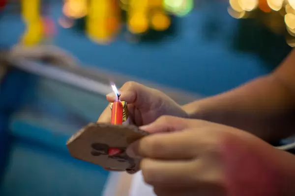Close Up Bokeh Photo of Person using a Lighter to ignite a Candle of a Floating Paper Lantern in Hoi An, Vietnam