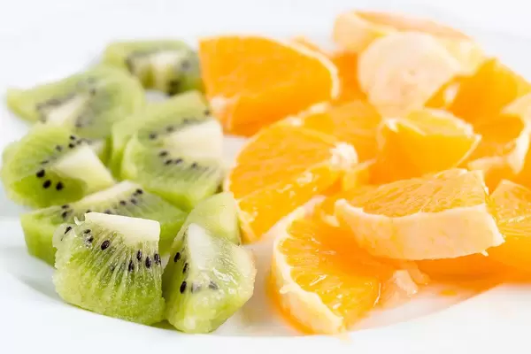 Close Up Bokeh Photo of Sliced Kiwi and Oranges on a Plate on White Background