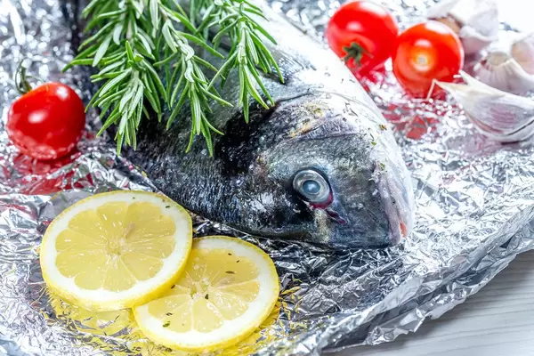Close - up Dorado fish with rosemary, lemon slices and tomatoes on foil (Flip 2019)