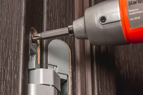 Close-up, electric screwdriver secures the door hinge