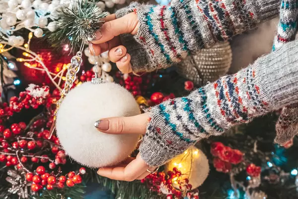 Close-up, female hands with a white ball decorate the christmas tree