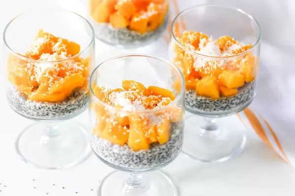 Close Up Food Photo of Chia Seed Pudding with Fresh Mango Cubes and Coconut Rasps in Glass Cups on White Background