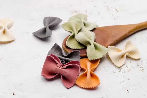 Close Up Food Photo of colorful Farfalle Bow Tie Pasta on a Wooden Spoon on White Wooden Background