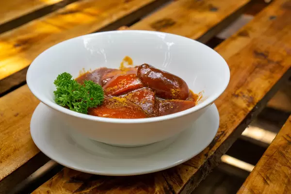 Close Up Food Photo of Currywurst with authentic German Bratwurst and homemade Curry Sauce in a White Ceramic Bowl with Curry Powder and Parsley at a German Restaurant