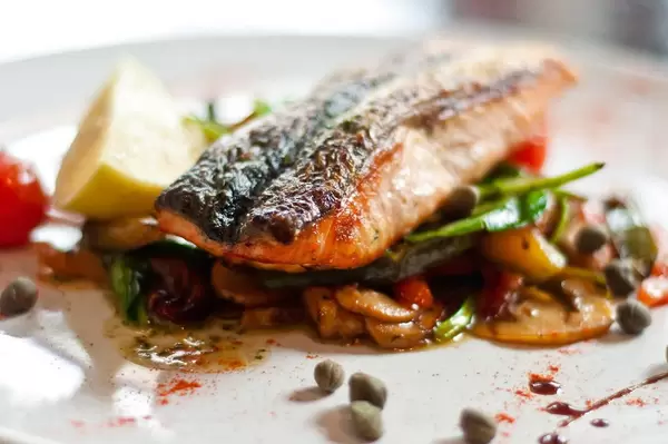 Close Up Food Photo of Delicious Pan Fried Fish on different Vegetables on White Plate at a fancy Restaurant