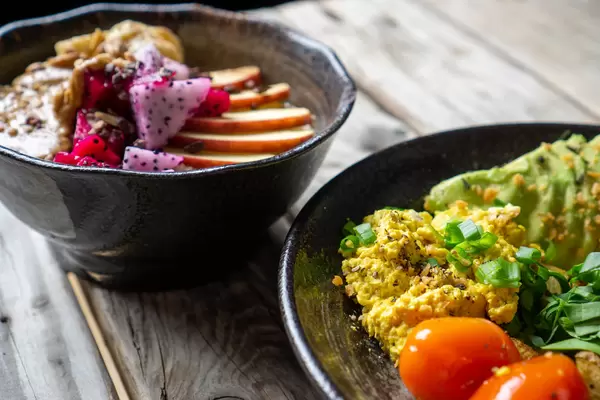 Close Up Food Photo of Healthy Vegan Breakfast with Scrambled Tofu, Cherry Tomatoes and Avocado with Porridge Bowl in the Background on a Wooden Table