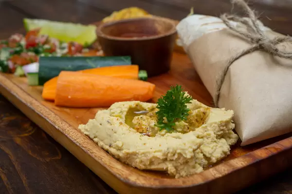 Close Up Food Photo of Homemade Hummus on a Wooden Lunch Plate with Raw Vegetables, Quinoa Toamto Salad and Tortilla Kebab Wrap