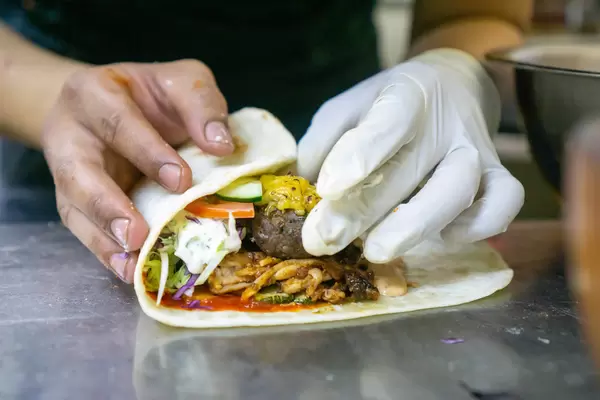Close Up Food Photo of Kitchen Chef rolling a Doner Durum Kebab Roll with Grilled Lamb, Cheese, Zucchini, Tomatoes, Cucumber, Cabbage, Tzatziki and Cocktail Sauce on a Kitchen Countertop