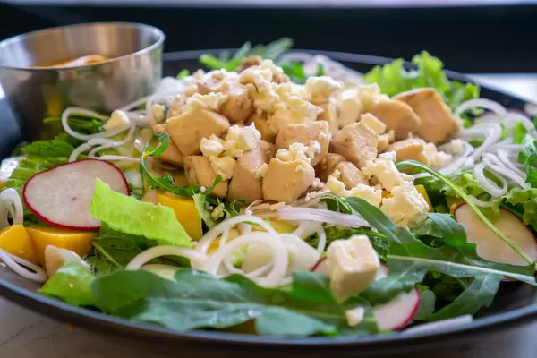 Close Up Food Photo of Mango Curry Chicken Salad with Grilled Chicken Breast, Feta Cheese, Arugula and Onions on a Ceramic Plate