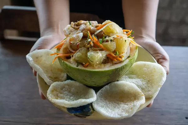 Close Up Food Photo of Person holding Plate of Pomelo Salad with Peanuts, Shrimps, Carrots and Shrimp Chips