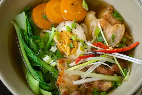 Close Up Food Photo of Ramen Soup with Fresh Vegetables, Egg, Pork and Chili in a Ceramic Bowl