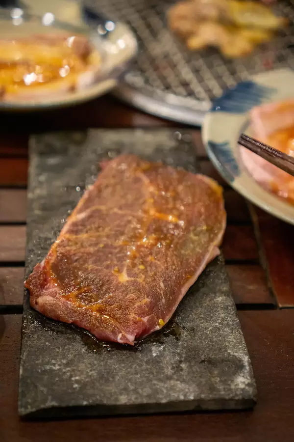 Close Up Food Photo of Raw Beef Steak on a Stone Plate next to a Table Barbecue Grill at a Restaurant