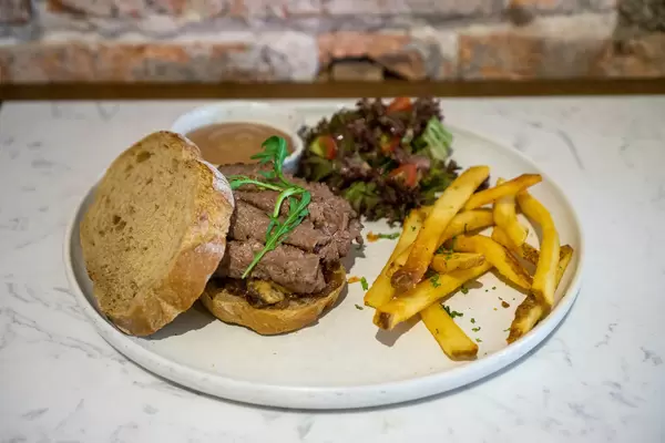 Close Up Food Photo of Slices of Steak with Caramelized Onions on Bread Slices with French Fries and Salad on a White Ceramic Plate