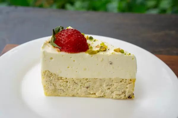 Close Up Food Photo of Small Piece of Cheesecake topped with Strawberry and Pistachio on a White Plate