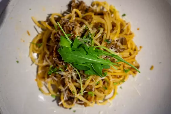 Close Up Food Photo of Spaghetti Bolognese topped with Grated Cheese and Arugula on a White Ceramic Plate