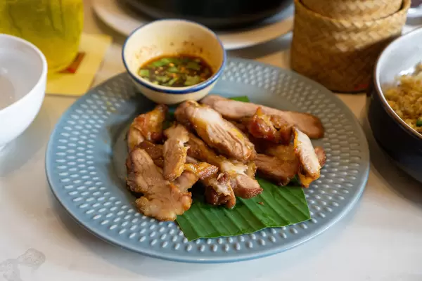 Close Up Food Photo of Thai Grilled Pork Neck Kor Moo Yang on Banana Leaves with Chili Sauce in a Restaurant