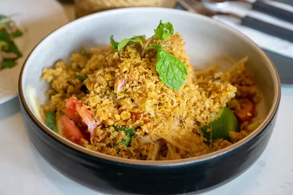 Close Up Food Photo of Thai Spicy Papaya Salad Som Tam with Peanuts, Chili, Tomatoes topped with Fried Catfish in a Restaurant