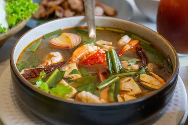 Close Up Food Photo of Tom Yum Thai Soup with Fresh Shrimps, Cilantro, Mushrooms and other Vegetables in a Ceramic Pot with Ladle