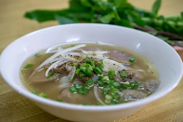 Close Up Food Photo of Vietnamese Noodle Soup Pho Bo with Fresh Herbs in the Background