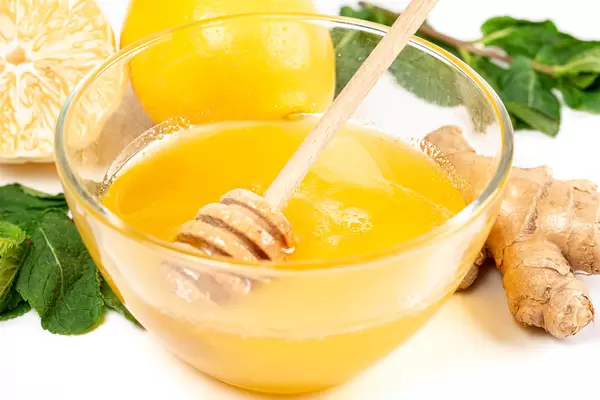 Close-up, fresh honey in a glass bowl on a white background with ginger and mint leaves