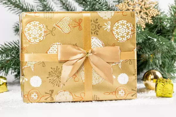 Close-up golden christmas gift with branches of a christmas tree behind