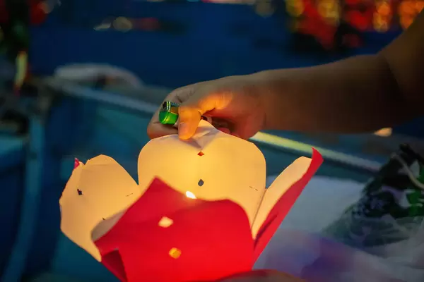 Close Up Night Photo of Person holding a Floating Paper Lantern with a lit up Candle in one Hand with a Lighter in Hoi An, Vietnam