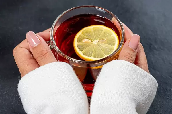 Close-up of a Cup of black tea with a piece of lemon in women's hands (Flip 2019)