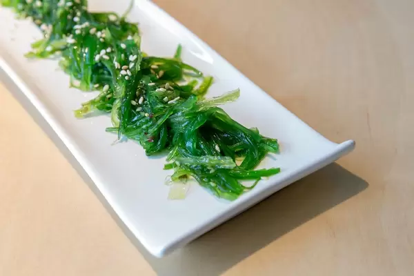 Close-up of a green vegan seaweed salad "Goma Wakame" with sesame seeds, in Japanese restaurant, on a bright wooden table