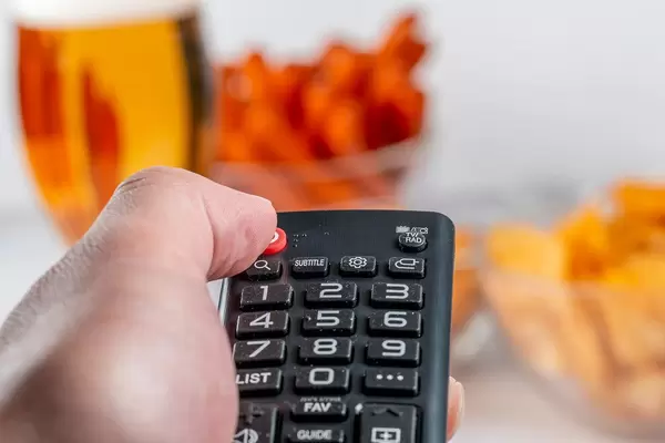 Close-up of a hand with a TV remote against the background of snacks and beer