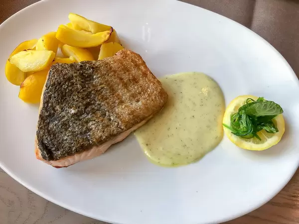 Close-up of a healthy lunch with grilled salmon fish fillet with herb dip, lemon slice and potato wedges