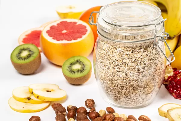 Close-up of a jar of oatmeal and slices of fresh colorful fruits on a white background with nuts