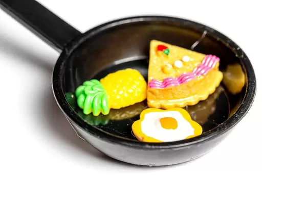 Close-up of a magnet toy frying pan with an egg, a piece of cake and a pineapple