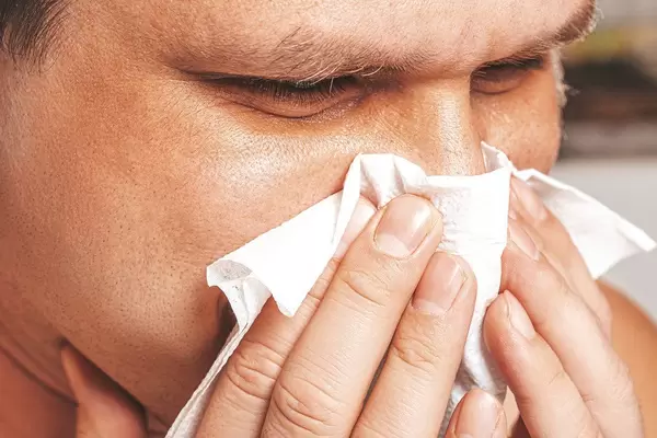 Close-up of a man with a runny nose holding a napkin near his nose