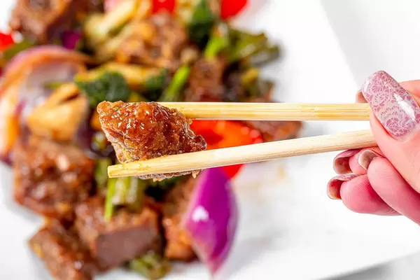 Close-up of a piece of baked beef in wooden chopsticks (Flip 2020)