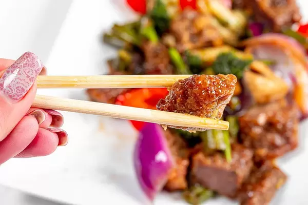 Close-up of a piece of baked beef in wooden chopsticks