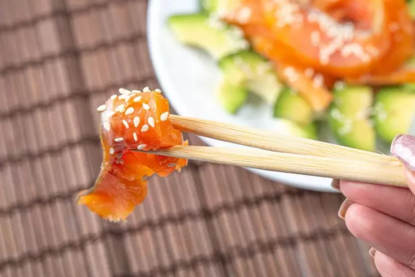 Close-up of a piece of smoked salmon with sesame seeds on chopsticks (Flip 2020)