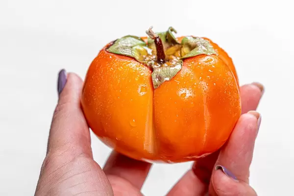 Close-up of a ripe orange persimmon in a woman's hand