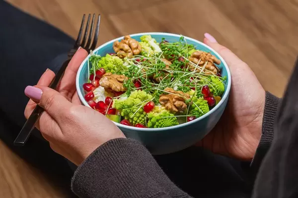Close-up of a vegetable salad with nuts and micro greenery in a woman's hands with a black fork. Dietary food (Flip 2020)