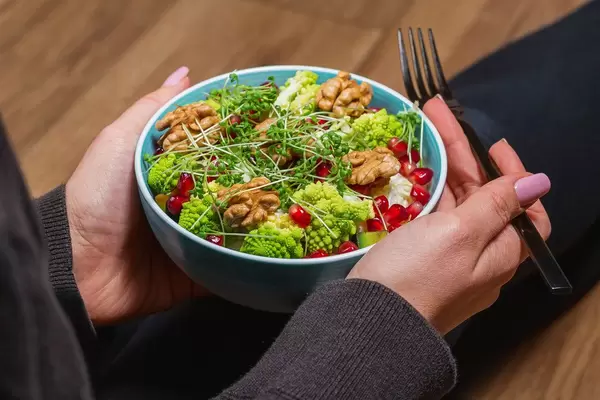 Close-up of a vegetable salad with nuts and micro greenery in a woman's hands with a black fork. Dietary food