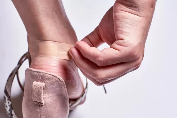 Close up of a woman foot in highheels putting a plaster on her heel