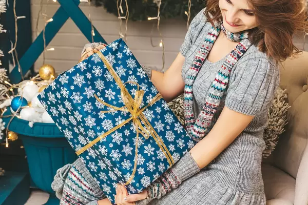 Close-up of a wrapped big christmas present in the hands of a girl sitting on an armchair